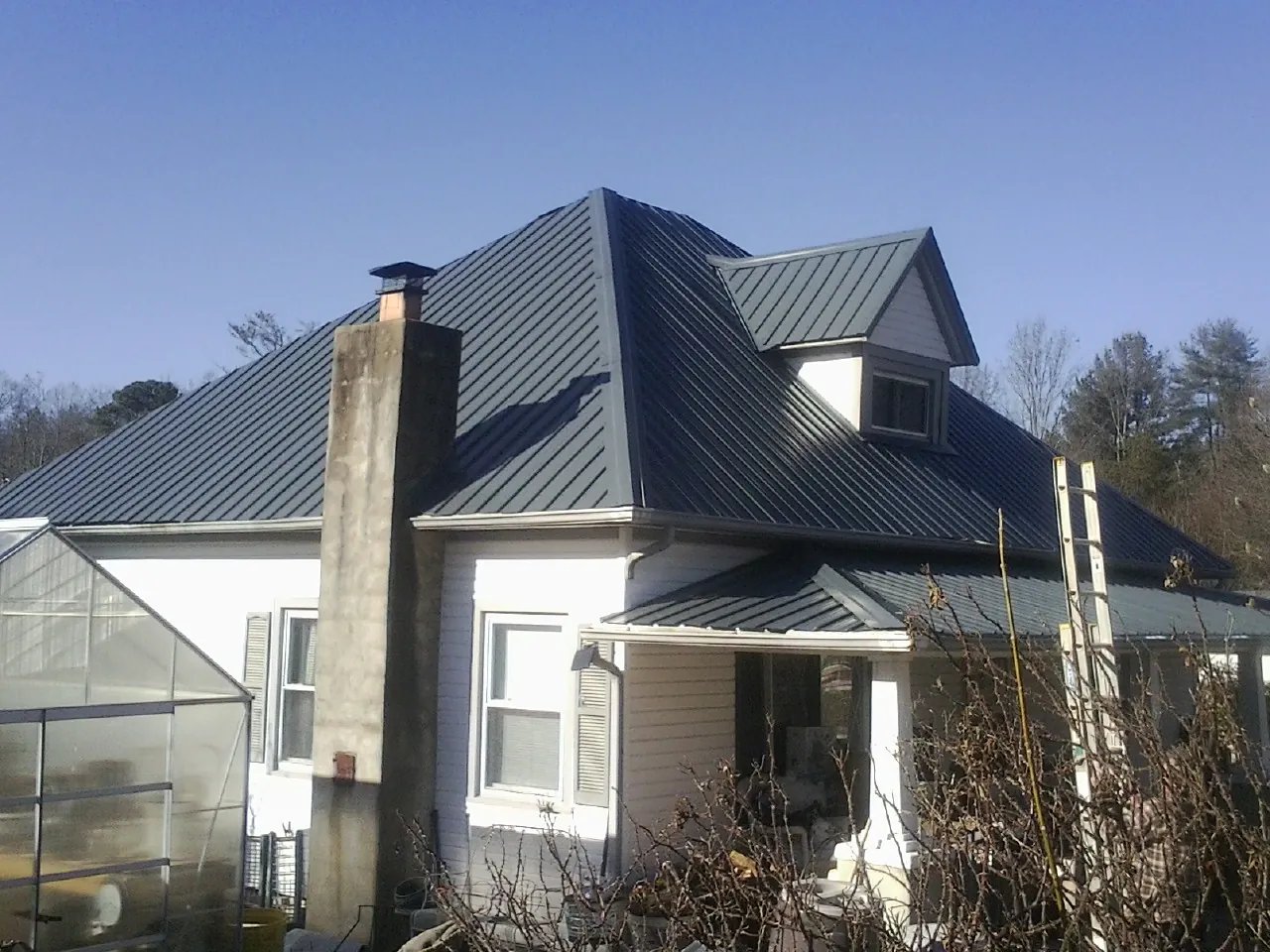 Dark blue standing seam metal roof on a white farmhouse with dormer — Slate & Tile Roof Repair by Roofing Brothers in Apex