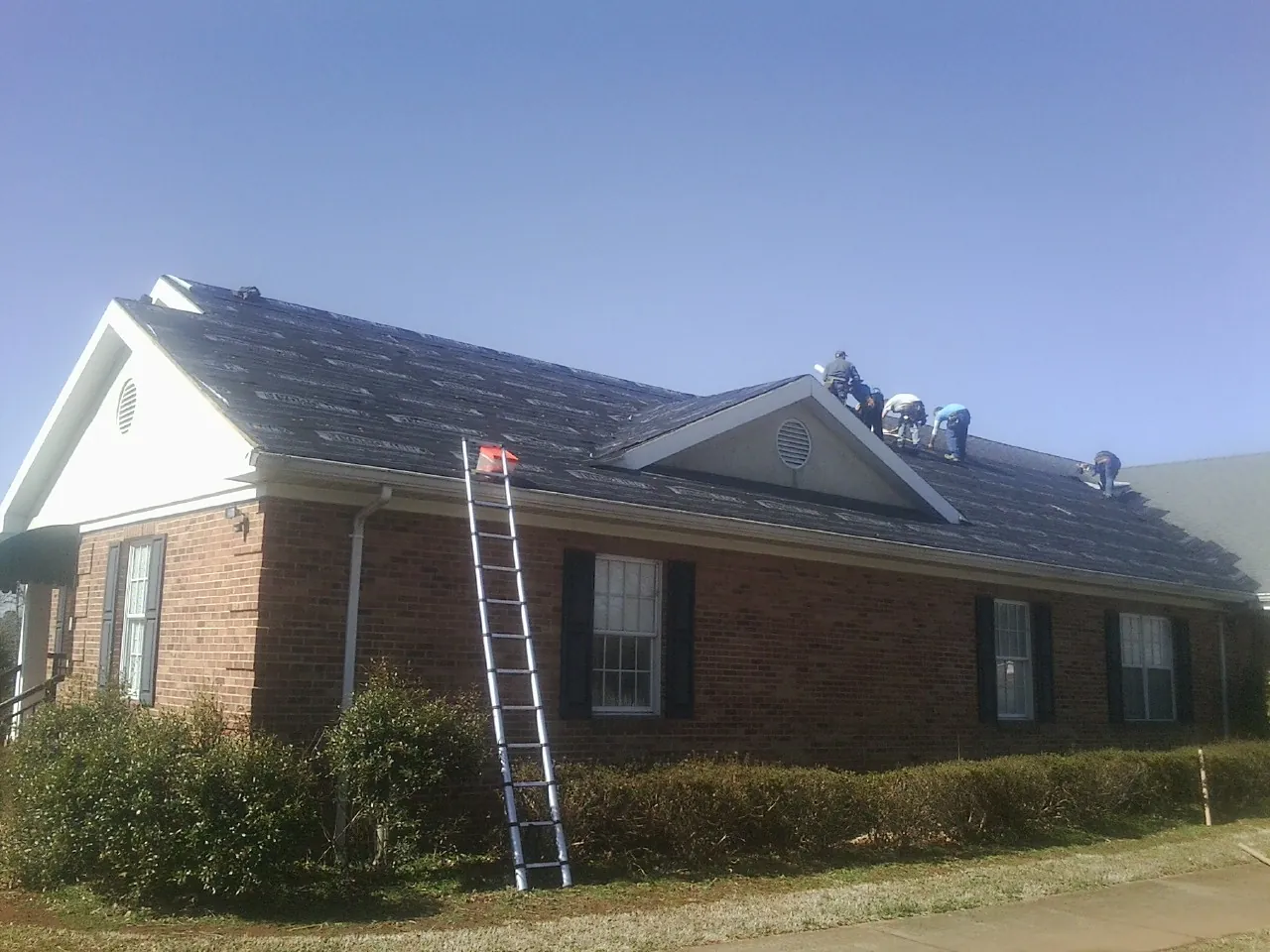 Crew tearing shingles off a brick ranch roof with a ladder set — Emergency Roof Repair work by our crew in Apex