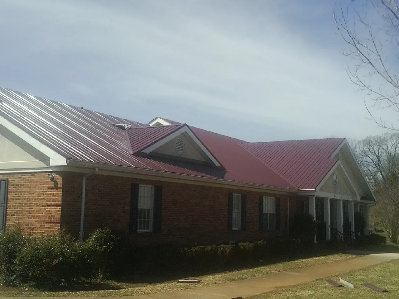 Red metal roof with gabled entries on a long brick building, from a Hail Damage Roof Repair job in Apex