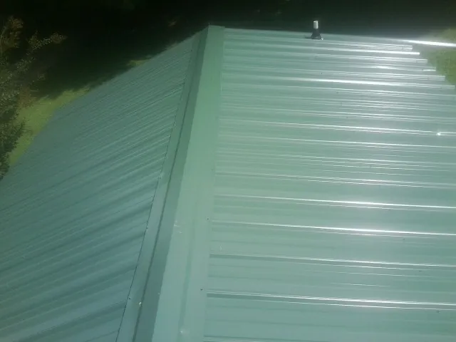 New green metal panels meeting at the ridge of a roof — Flat Roof Repair work by our crew in Apex