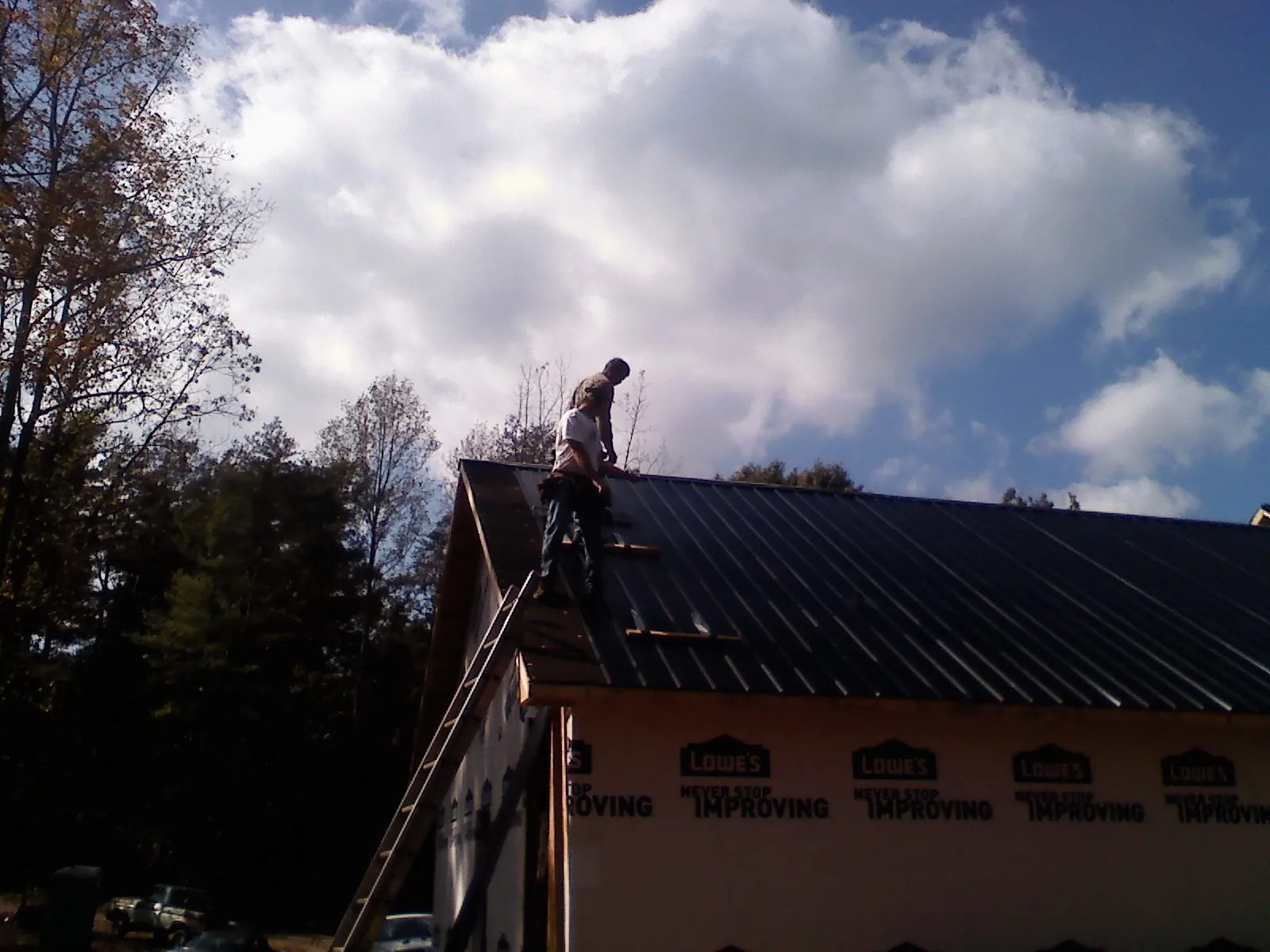 Roofer fastening dark metal panels high against a cloudy sky, from a Roof Inspection job in Apex