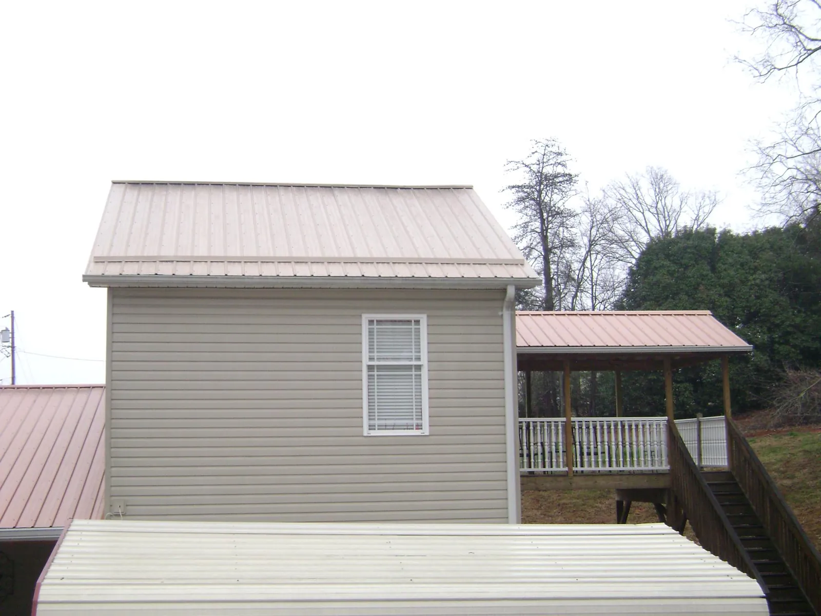 Tan metal roofs on a two story addition and attached porch, from a Roof Replacement job in Apex